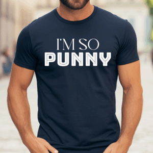 Man wearing a dark navy blue t-shirt with bold white text that reads “I’M SO PUNNY.” The design uses a mix of elegant and block lettering styles. The man stands casually outdoors with his hands in his pockets, and the background shows a softly blurred street scene.